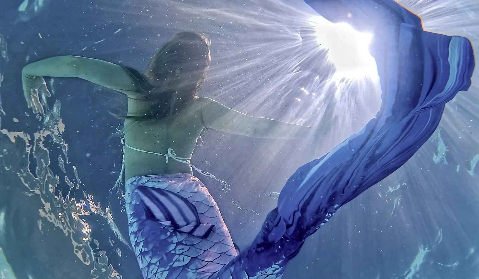 Mermaid and violet-blue tail beneath beams of sunlight